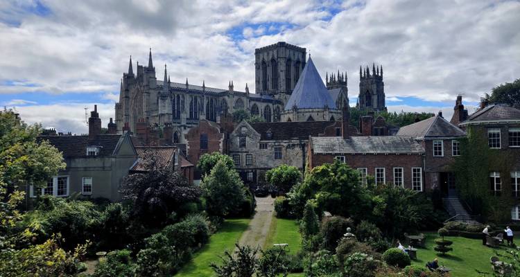 Les tours gothiques de la cathédrale d'York dominent un jardin luxuriant et un paysage urbain de briques rouges sous des nuages mouchetés