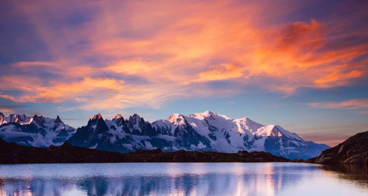 Impresionantes picos montañosos con nieve bajo un cielo vibrante de atardecer.
