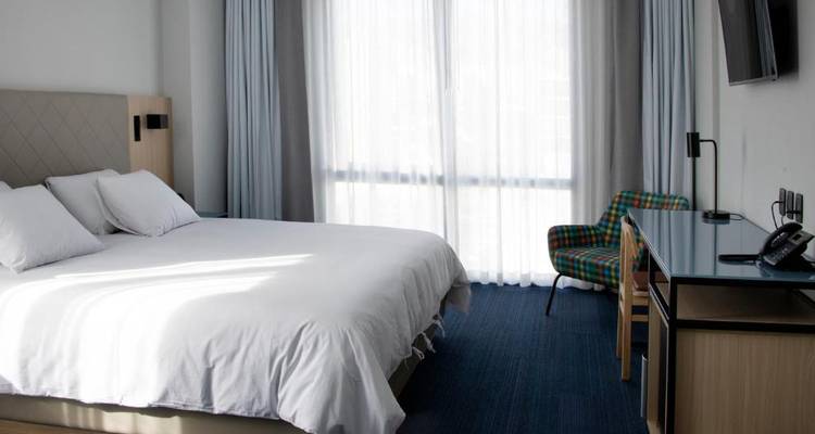 Chambre d'hôtel moderne avec un grand lit près d'une fenêtre lumineuse.