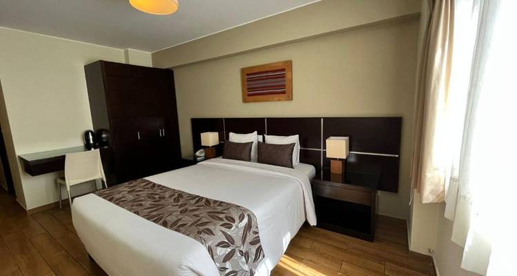 Hotelzimmer mit einem ordentlich gemachten Bett, einem Schreibtisch und einem Fenster mit Vorhängen.