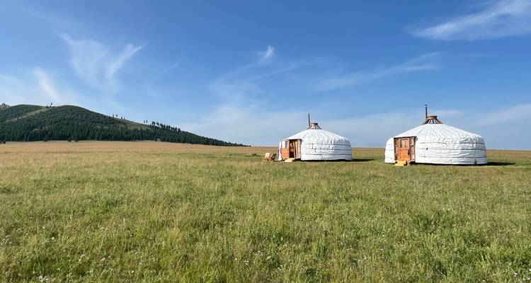 Deux yourtes blanches se dressent seules sur une vaste steppe verte sous un ciel mongol bleu et clair