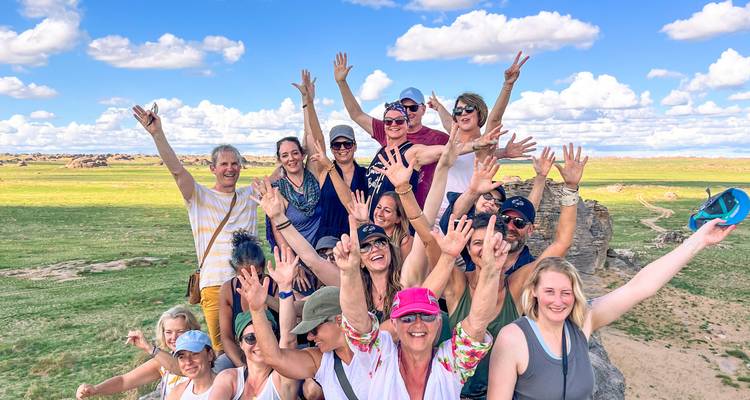 Un groupe de touristes joyeux lève les mains en signe de célébration sur un vaste paysage de prairies mongoles