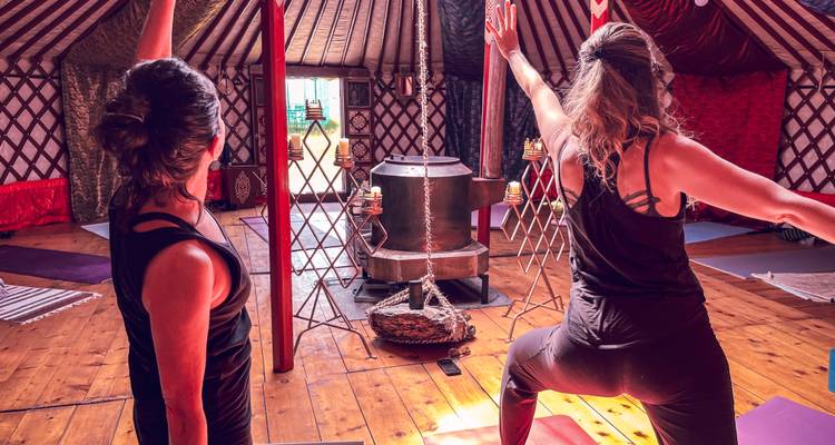 Deux femmes pratiquent des postures de yoga à l'intérieur d'une yourte confortable éclairée par une chaude lumière du soleil