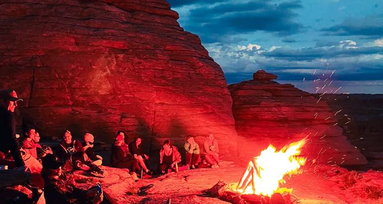 Des voyageurs se rassemblent autour d'un feu de camp rugissant au milieu de rochers rouges escarpés au crépuscule