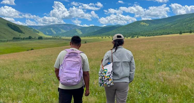 Deux randonneurs contemplent une large vallée verdoyante sous un ciel d'été lumineux