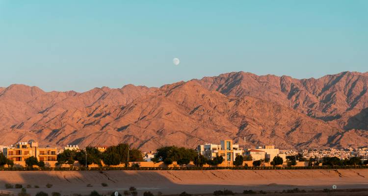 Arid mountain range at dusk with a half moon above a modern desert town