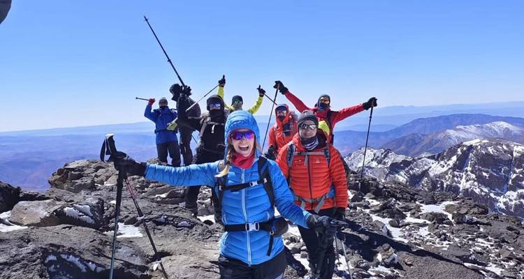 Personas con bastones de senderismo en una cima nevada de montaña, celebrando.