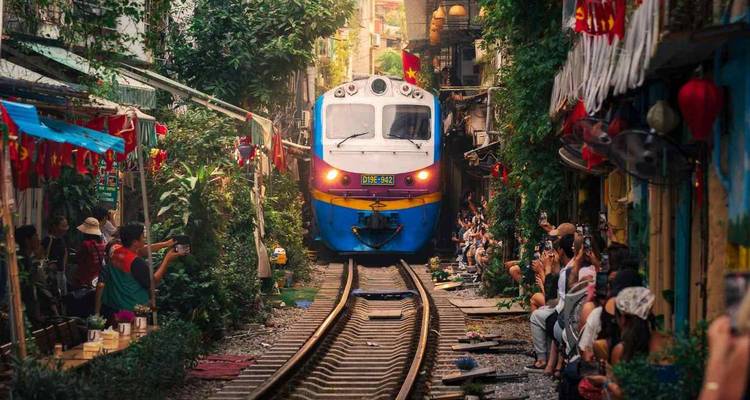 Een trein die door een smalle straat rijdt met winkels en mensen langs de kant.