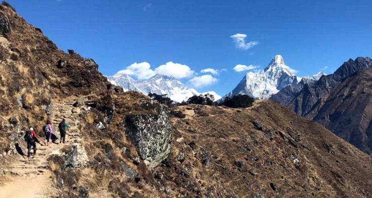 Randonneurs sur un sentier de montagne avec des sommets enneigés.
