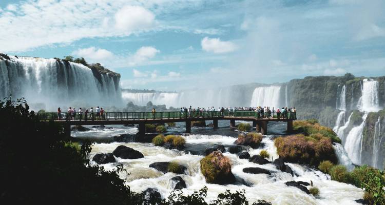 Paseo marítimo largo lleno de visitantes entre las rugientes Cataratas del Iguazú y el río espumoso abajo.
