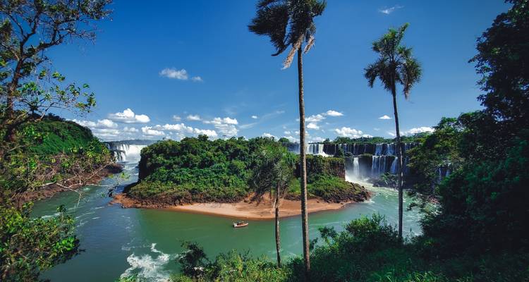Vista panorámica de isla exuberante y cataratas de Iguazú de múltiples niveles bajo un cielo azul brillante.