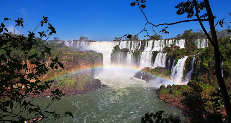 Dramática herradura de las Cataratas del Iguazú con niebla y un arcoíris vivido arqueándose sobre el agua turbulenta.