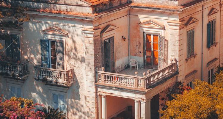 Nahaufnahme eines eleganten terracottafarbenen Villabalkons im Schatten von Bäumen an der Amalfiküste.