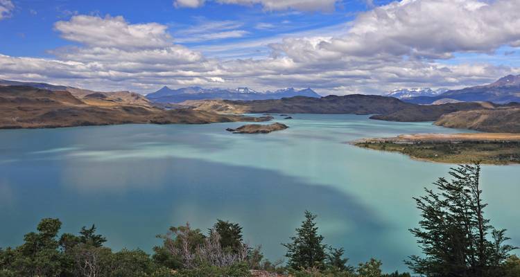 Amplio panorama de un lago turquesa salpicado de islas rodeado de colinas ondulantes de la Patagonia