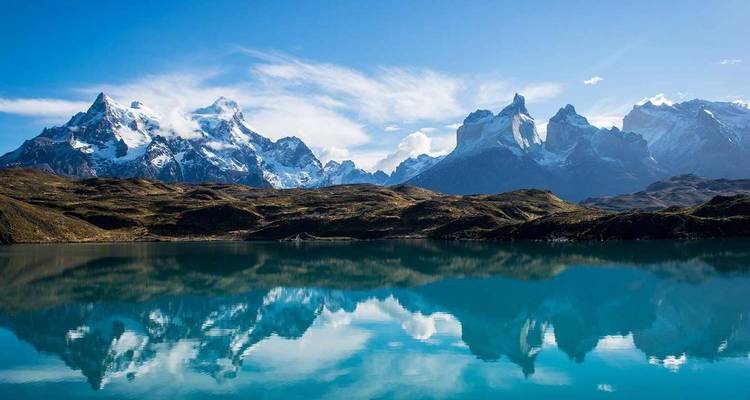 Los icónicos picos dentados de Torres del Paine reflejados perfectamente en un lago azul tranquilo bajo cielos despejados