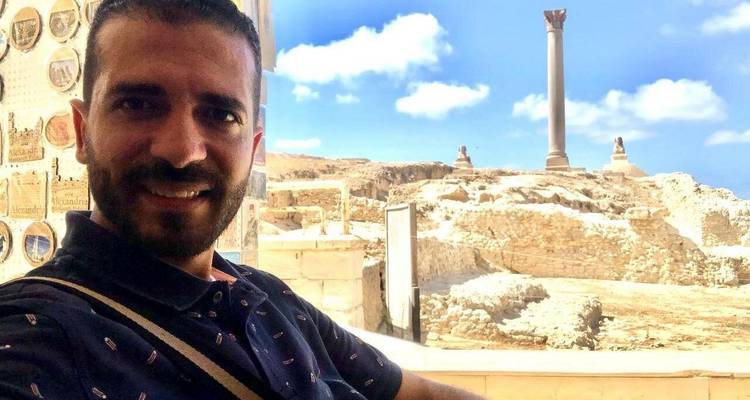 Un hombre tomándose una selfie con el telón de fondo de una columna antigua y artefactos.