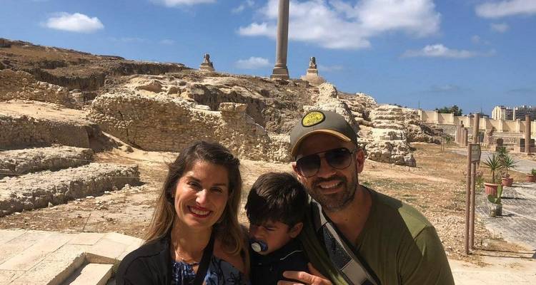 Una familia posando felizmente frente a una columna antigua con ruinas.