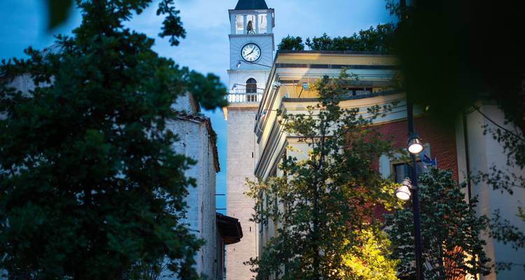 Evening view of Tirana’s clock tower rising above leafy streets and softly lit buildings.