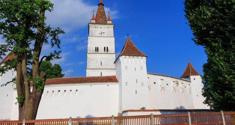 White defensive walls and tile-roofed towers of the Prejmer fortified church beneath a deep blue sky.