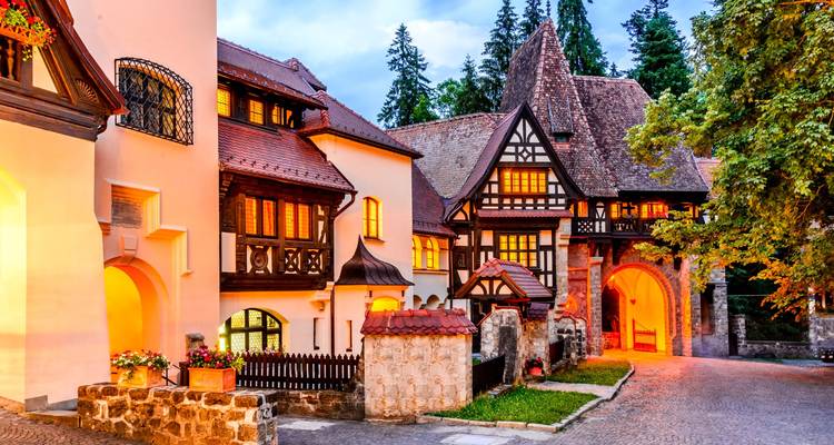 Warm verlichte houten villa binnen het domein van kasteel Peleș, omringd door naaldbos bij schemering.