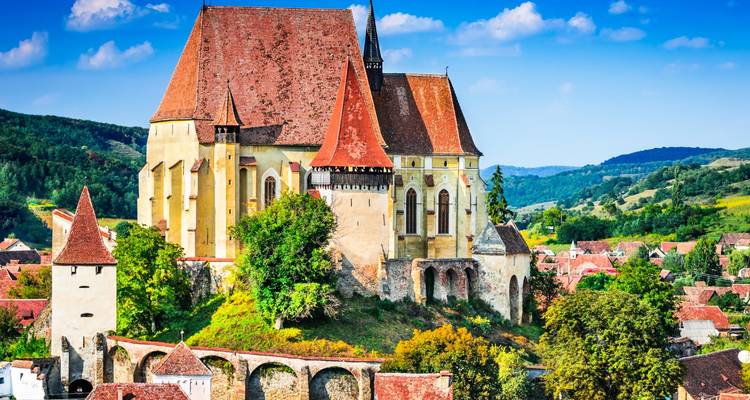 Fortified hilltop church with steep red roofs towering above a medieval Transylvanian village and rolling green hills