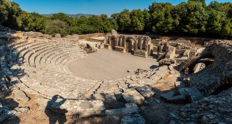 Stone amphitheatre ruins set in a forest clearing with curved seating and ancient arches
