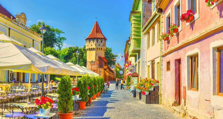 Lively café street lined with pastel buildings and medieval tower basking in bright sunshine.