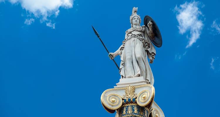 Marble statue of the goddess Athena holding spear and shield against a vivid blue sky.