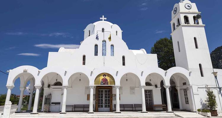 Whitewashed Greek Orthodox church with arches, domes, and a bell tower against a deep blue sky