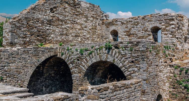 Arches et murs de pierre anciens d'une fortification en ruine sous un ciel bleu éclatant.