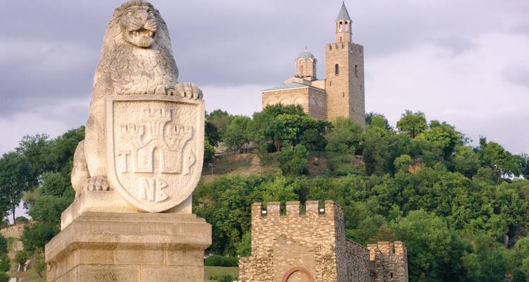 Forteresse au sommet d'une colline avec statue de lion et verdure environnante.