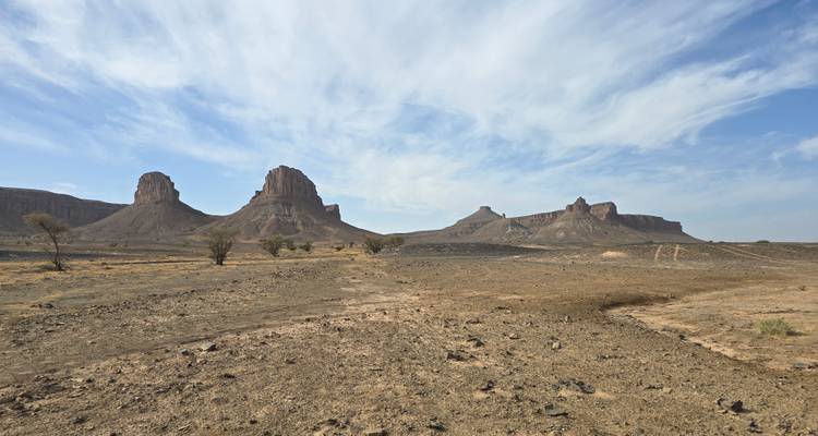 Droge woestijnvlakte met geïsoleerde mesa-achtige rotsformaties onder ijle wolken