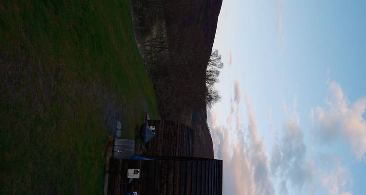 Fila de cabañas de glamping de madera en ladera herbosa al anochecer con cielo pastel.