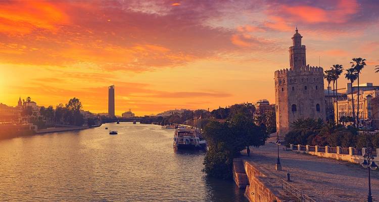 Golden sunset over the Guadalquivir River with the Torre del Oro and vibrant sky reflected in the water.