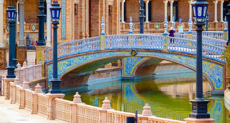 Colorful ceramic-tiled bridge crossing the canal at Plaza de España with ornate lampposts.