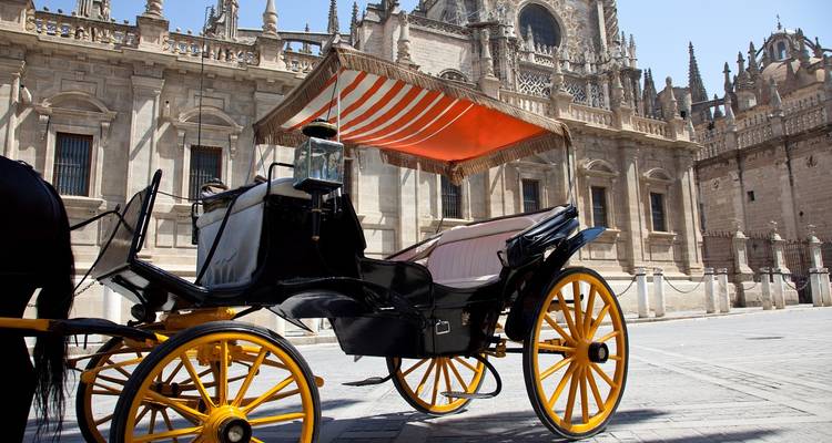 Classic black horse-drawn carriage with bright yellow wheels parked beside Seville Cathedral.
