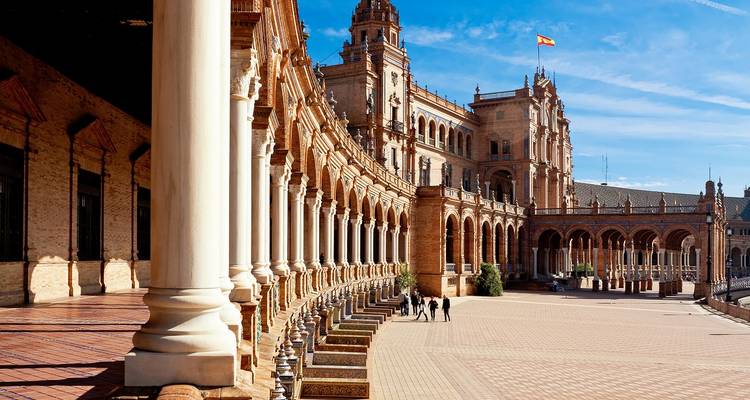 Grand curved colonnade of Plaza de España with visitors walking across its patterned tiles.