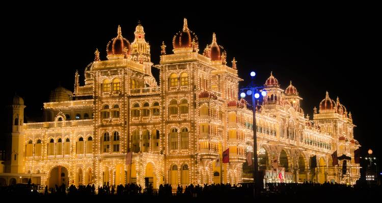 Mysore Palace verlicht in de nacht met een menigte ervoor.