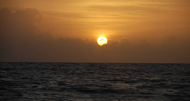 Zon die ondergaat boven een donkere, zacht golvende oceaan met wolken aan de horizon