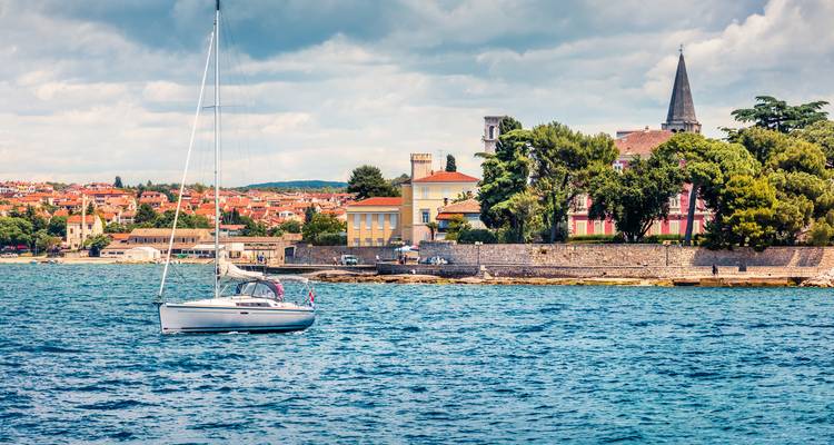 Pueblo costero con casas vibrantes y un velero en aguas azules cristalinas.