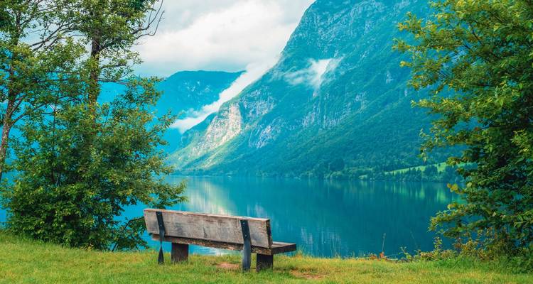 Banco vacío con vista a un lago tranquilo con montañas al fondo.