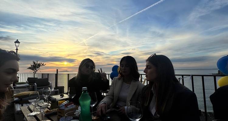 Groupe de femmes assises à une table avec vue sur le coucher de soleil au-dessus de la mer.