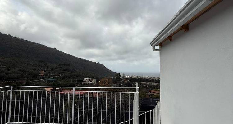Vue depuis un balcon surplombant un paysage vallonné sous un ciel nuageux.