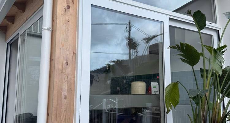 Bâtiment moderne aux murs de verre avec végétation environnante par temps nuageux.