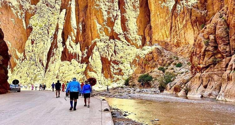 Reizigers die naast hoge gouden canyonwanden wandelen met een beek die licht reflecteert