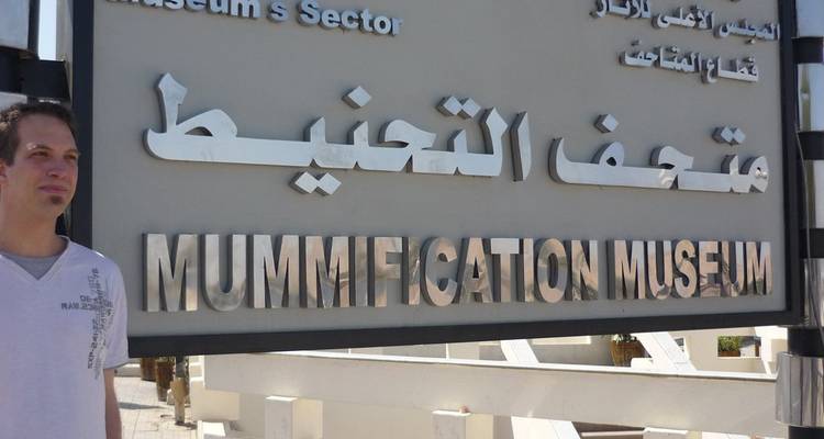 Hombre parado cerca de un letrero que dice 'Museo de Momificación' con texto en árabe.