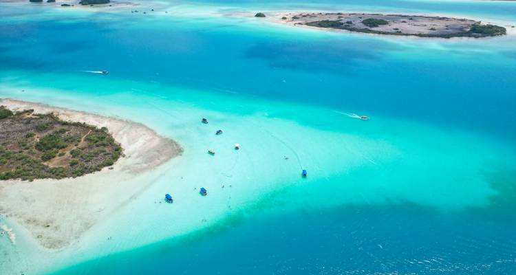 Stunning aerial of bright turquoise lagoon dotted with small sandy islets and leisure boats.
