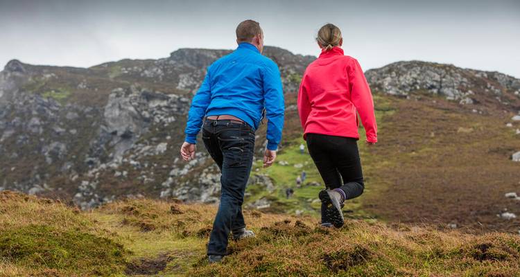Couple in bright jackets hike uphill across heather-covered slopes in Donegal
