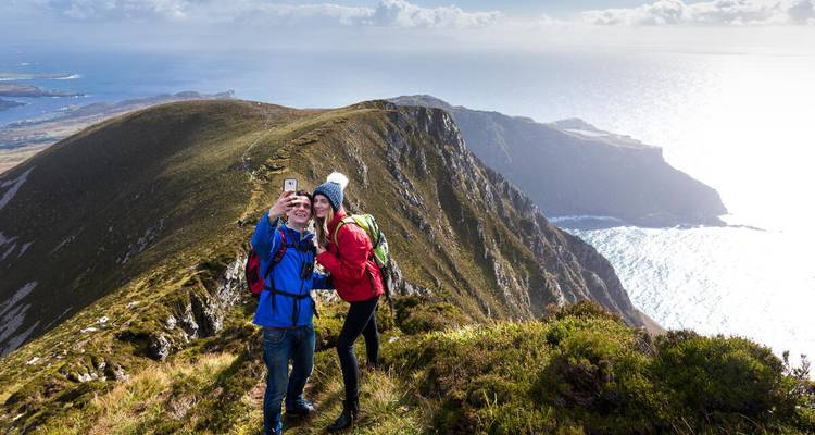 Young couple takes a selfie atop high sea cliffs with sparkling Atlantic backdrop