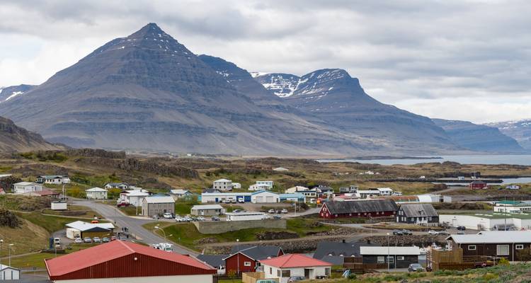 Cloudy day view of fjord-side hamlet framed by steep volcanic mountains with patches of snow